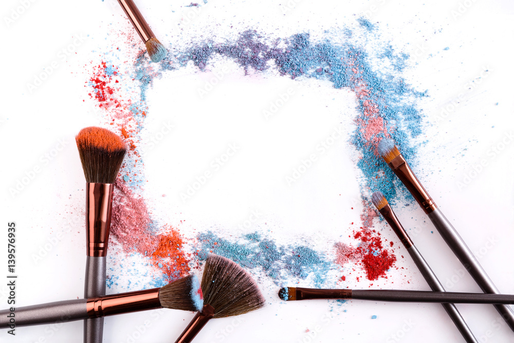 Wall mural Makeup brushes with blush or eyeshadow of pink, blue and coral tones sprinkled on white background