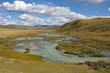 Fototapeta na wymiar White wide river on a background of rocky hills under white clouds and blue sky, Plateau Ukok, Altai mountains, Siberia, Russia