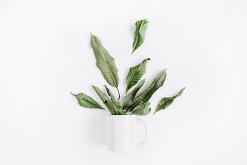 Blank template of white mug and green leaves bouquet on white background. Flat lay, top view.