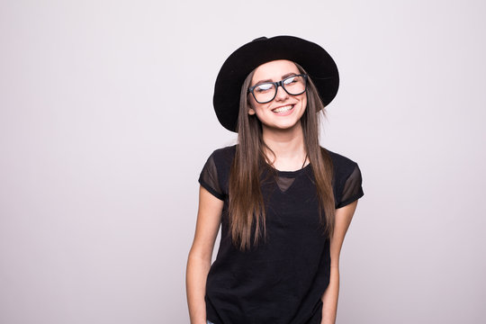Fashionable brunette wearing bright black clothes holding her hat with eyesglasses isolated on grey