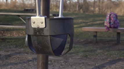 Empty swing at playground with book bag of school child sitting on bench, abandoned.
