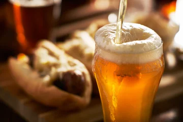 Papier Peint photo autocollant Bière verser de la bière ambrée dans une tasse avec des bratwursts en arrière-plan