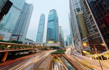 Fototapeta premium Malowniczy widok na róg ulicy w Hongkongu z wieżowcami biurowymi w tle i ruchliwymi drogami w godzinach szczytu ~ Piękny pejzaż centrum Hongkongu z panoramą nowoczesnych drapaczy chmur