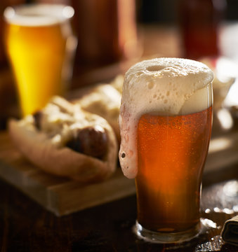 IPA beer with overflowing foamy head in mug served with bratwursts