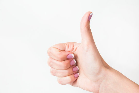 Closeup of one female caucasian hand isolated on white background. Young woman shows thumb up as sign of likeness. Horizontal color photography.