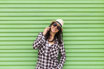 Happy beautiful woman talking on the phone over green background. Wearing hat and sunglasses.