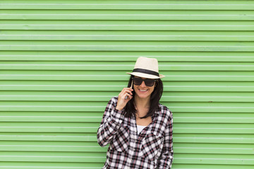 Happy beautiful woman talking on the phone over green background. Wearing hat and sunglasses.