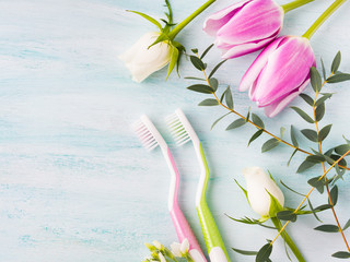 Two pastel toothbrushes with flowers herbs over green textured background. Spring colors. Personal dental health care. Healthy couple concept