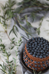 beautiful chocolate layered cake with open biscuits, decorated with fruit blueberries in a brown ceramic bowl on kitchen grey towel on white wooden background top view