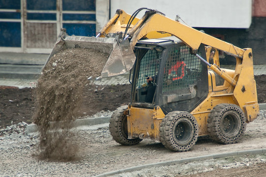 Yellow wheel skid-steer loader machine unloading gravel at construction area outdoors