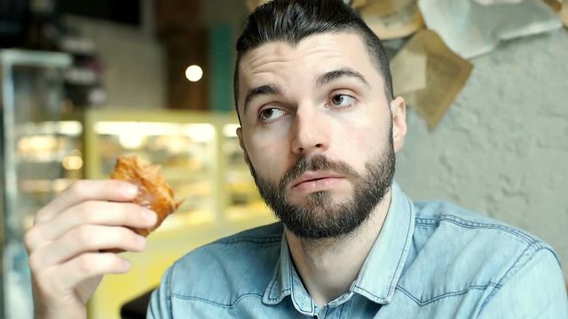 Handsome man holding croissant and speaking to someone in the cafe
