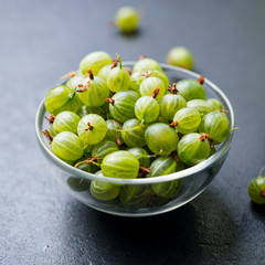 Fresh gooseberries in glass bowl on black stone slate background.