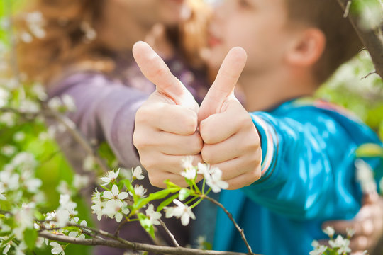 Happy family of young mom and 9 years old son having fun outdoors in spring blooming garden near. Close up of female and child hands with thumbs up. Allergy free concept. Horizontal color photography.