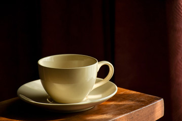 Empty coffee cup under afternoon sunlight prepared for coffee time. Dark room corner background.