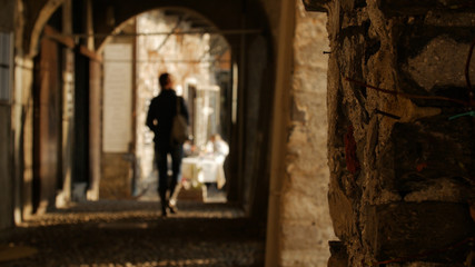 Young woman walking through the arches of the historical buildings away from the camera.
