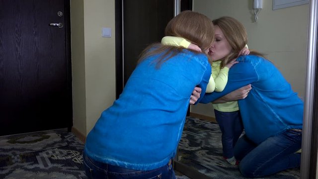 Loving woman hug her daughter girl near mirror and simper