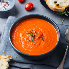 Tomato soup in a black bowl on grey stone background.
