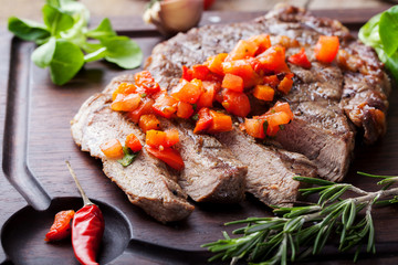 Beef steak well done with tomato and pepper salsa on a wooden background.