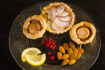 Pirogena-baskets with apple, red currant and sugar powder, almonds and lemon. On a transparent plate (black background).