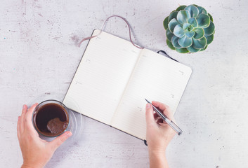 Open empty notebook on white wooden table with cup of coffee, succulent flower and someones hands