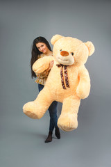 Young beautiful girl with big teddy bear soft toy happy smiling and playing on grey background