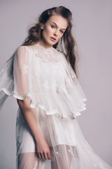 Portrait of a beautiful, gentle girl blonde in an image of the bride. Dressed in a light white lace dress. The beauty of the face. Photos in the studio on a gray background.