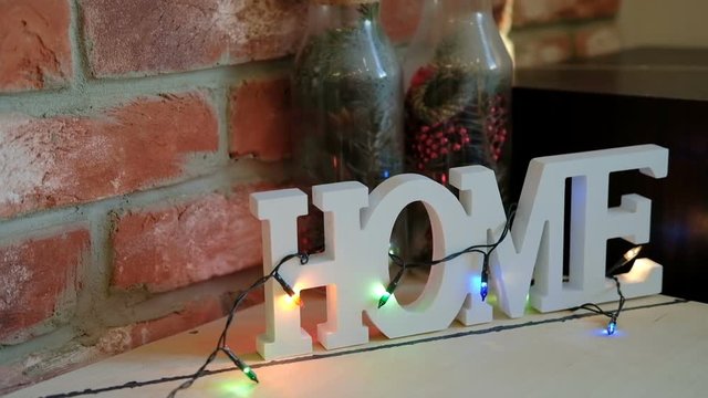 Decoration house, toy Christmas in winter holidays indoors. New year decorating in corner glass bottle with cones from pine tree, fir-tree branches, red beads. On table large white letters word home