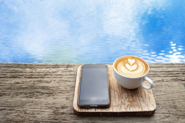 Morning coffee latte cup and smart phone with beautiful blue sky and puffy clouds reflecting on the...