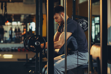 Naklejka na ściany i meble Handsome man doing biceps lifting barbell on bench in a gym