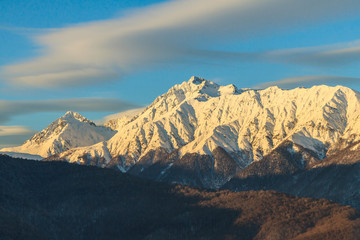 Beautiful winter mountain landscape of the Main Caucasus ridge with scenic snowy mountain peaks and blue sunset sky