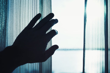 Hand opens tulle on window, blue toned