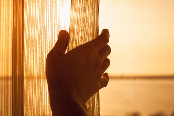 Hand opens tulle on window with sunlight