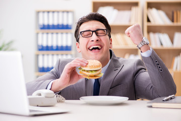 Fototapeta premium Hungry funny businessman eating junk food sandwich