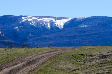 In the foreground is a dirt road leading to the snow-covered mountain tops.