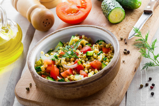 Delicious Israeli couscous Ptitim with vegetables on a white wooden table. Cooking of healthy vegetarian food for the meal. Traditional Moroccan cuisine.
