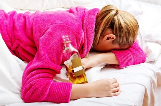 Young worried woman drinking alcohol in bed