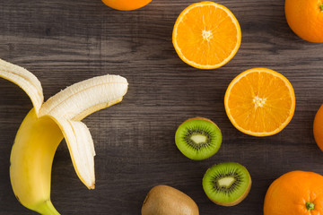 Banana with kiwi and orange on the wooden table in the kitchen. Healthy eating and lifestyle.