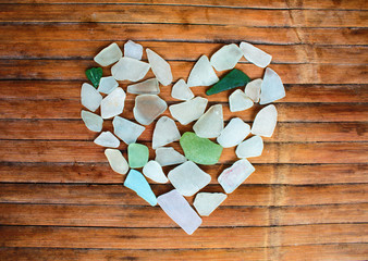 Seashore glass pebble heart on wooden background. Sugar glass mosaic for Valentine's Day.
