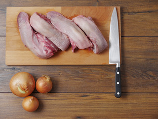 Still life: Raw pork tongues on a wooden cutting board, onions and knife, 