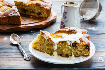 Piece of a homemade pear and chocolate cake with sweet sauce and icing sugar on a white plate on the wooden rustic table.