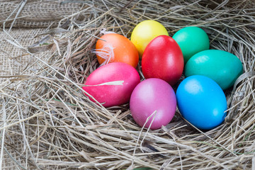 Colorful easter eggs in hay on wooden background