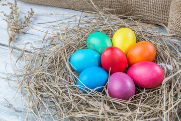 Fototapeta premium Colorful easter eggs in hay on wooden background