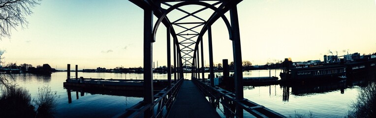 Panoramic view on the bridge from Entenwerder in Hamburg Germany, with the very calm Elbe, some houses and some trees in the background.  