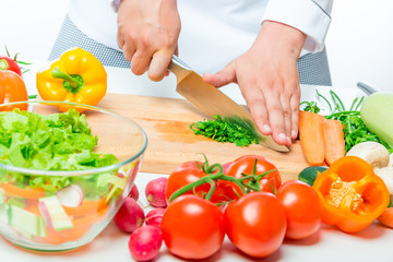 bowl with salad and fresh vegetables for cutting on a white table
