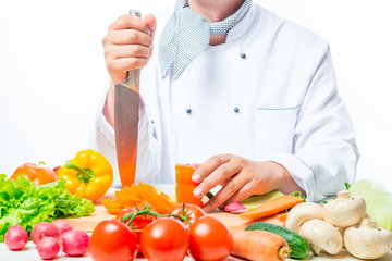 chef at the table with a knife cut fresh vegetables for salad