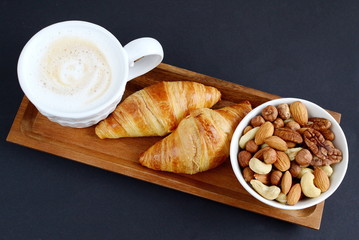 Cup of cappuccino, croissants and plate of nuts on the table