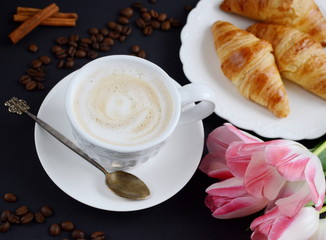 Cup of cappuccino and croissants with pink tulips on the table
