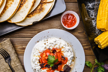 Quesadilla, salad with cottage cheese and tomatoes, two corn on wood table.