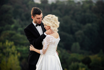 Sensual beautiful bride and handsome groom hugging tenderly on the background of the trees