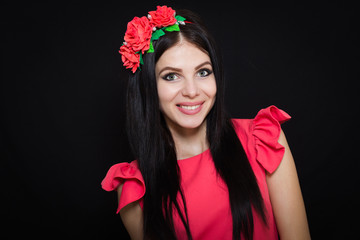 Fototapeta premium Woman with long black hair and wreath with red flowers on a dark background smiles. Close-up. Space for text